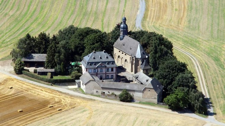 Eine historische Kirche umgeben von Feldern und Bäumen. Das Gebäude ist von einer ruhigen Landschaft umgeben.