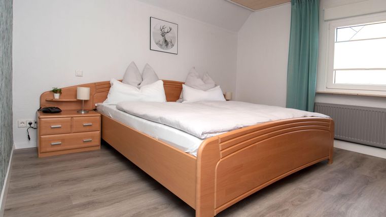 Ein gemütliches Schlafzimmer mit einem großen Doppelbett und Kissen. Der Raum hat einen schlichten, modernen Stil mit Holzdetails und einer sanften Farbpalette.