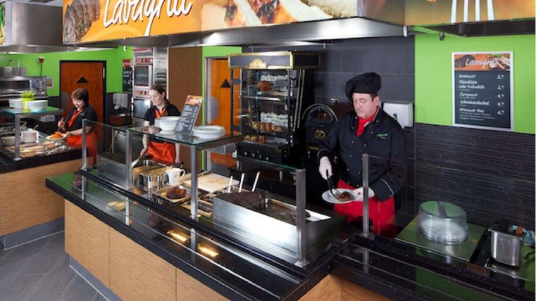 Ein modernes Restaurant mit einer Grillstation. Mitarbeiter bereiten Speisen in einer ansprechenden Umgebung vor.