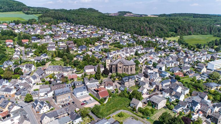 Eine malerische Landschaft mit vielen Häusern und einem großen Kirchengebäude im Zentrum. Die Umgebung ist von sanften Hügeln und grünen Feldern umgeben.