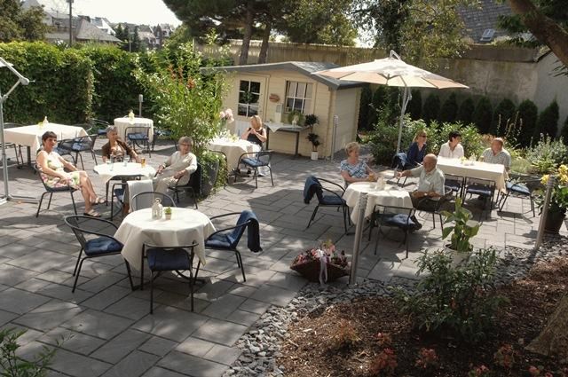 A cozy garden with table groups and sun umbrellas. Several people are enjoying their time outdoors.