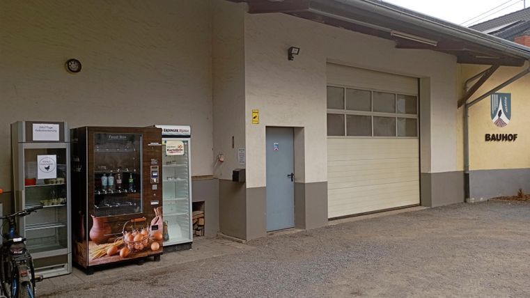 A building with a gray wall and an open garage. Next to the door are two vending machines.