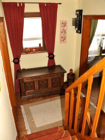 Ein heller Flur mit einem Holztisch und roten Vorhängen. Die Treppe führt nach oben und es gibt ein Fenster, das natürliches Licht hereinlässt.