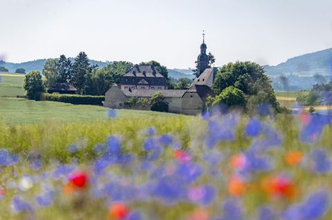 A picturesque landscape with a church and an old building in the background. In the foreground, colorful flowers are blooming.