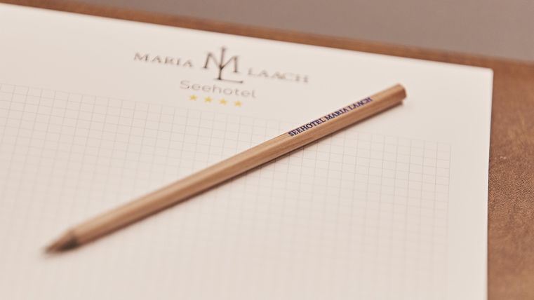 Ein Notizblock mit dem Logo von "Maria Laach" und ein Holzstift liegen auf einem Tisch. Der Block ist kariert und bereit zum Schreiben.