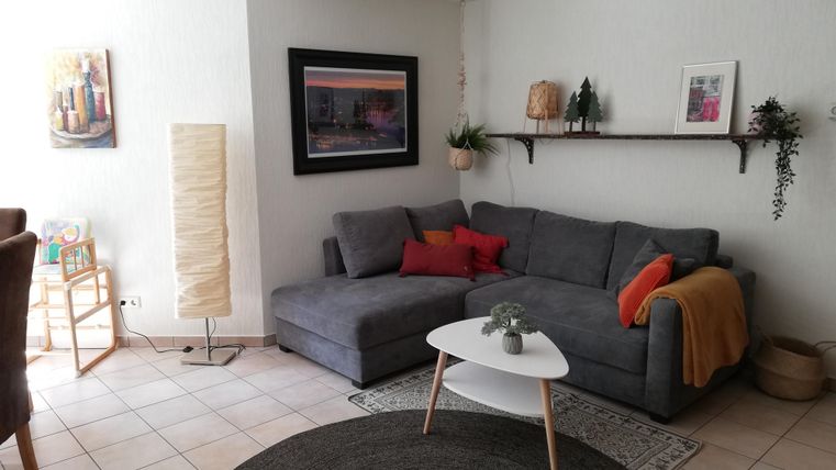 A modern living room with a gray sofa and a white coffee table. The room is bright and has decorative elements like plants and pictures on the walls.