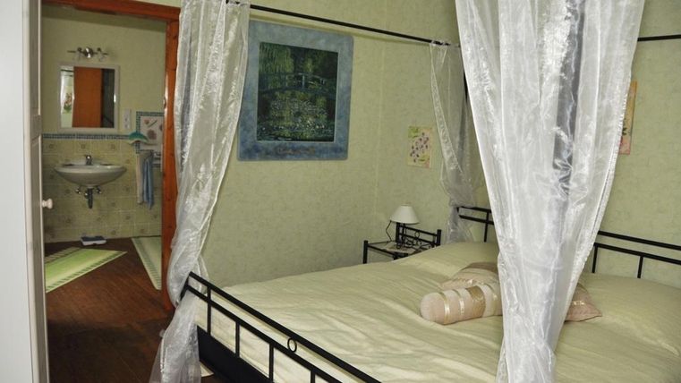 Ein gemütliches Schlafzimmer mit einem Doppelbett und einem Moskitonetz. Im Hintergrund ist ein Badezimmer mit einem kleinen Waschbecken sichtbar.
