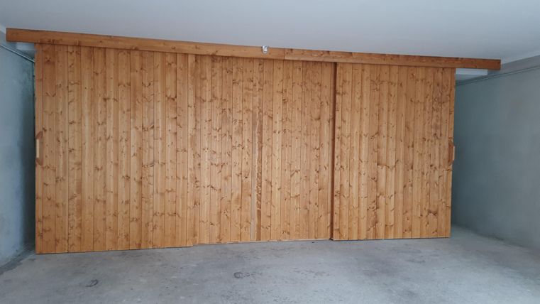 Eine Holzschiebetür in einer Garage. Der Raum ist schlicht und hat einen grauen Betonboden.