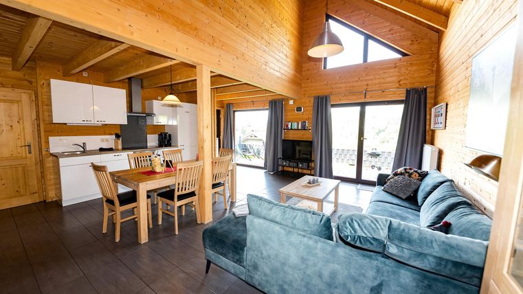 A modern wooden house with an open living kitchen. The bright room features large windows and a cozy seating area.