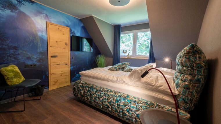 Ein modernes Schlafzimmer mit einem bunten Bett und Holzvertäfelung. Die Wände sind mit einem Naturmotiv dekoriert und sorgen für eine entspannte Atmosphäre.