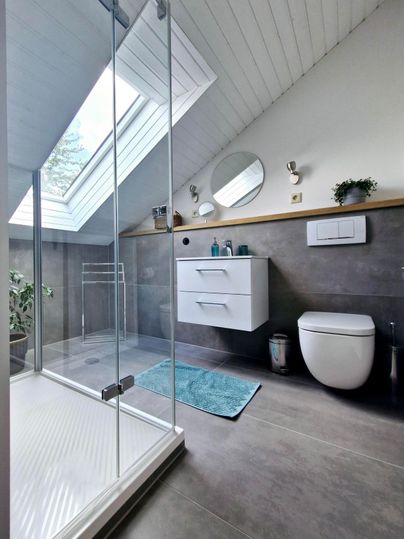 Ein modernes Badezimmer mit einer Dusche, einem Waschbecken und einem Fenster. Der Raum hat helle Farben und eine elegante Ausstattung.