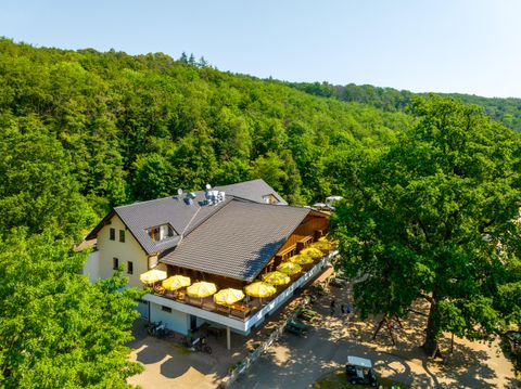 A cozy restaurant in the greenery with yellow sun umbrellas on the terrace. Surrounded by lush trees and a beautiful natural landscape.