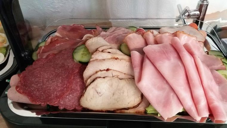 Eine Auswahl an verschiedenen Wurst- und Fleischwaren, schön angerichtet auf einem Teller. Es sind zudem einige Gurkenscheiben zu sehen.
