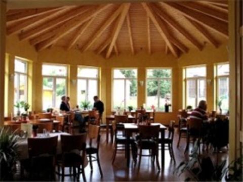 Ein gemütliches Restaurant mit großen Fenstern und Holzbalkendecke. Gäste sitzen an Tischen und genießen die Atmosphäre.