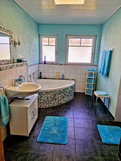 Ein modernes Badezimmer mit blauen Wänden und einer runden Badewanne. Es gibt weiße Fliesen, Handtücher und eine kleine Ablage.